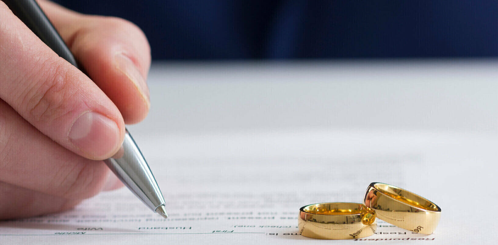 Person signing divorce papers with two wedding rings on the papers
