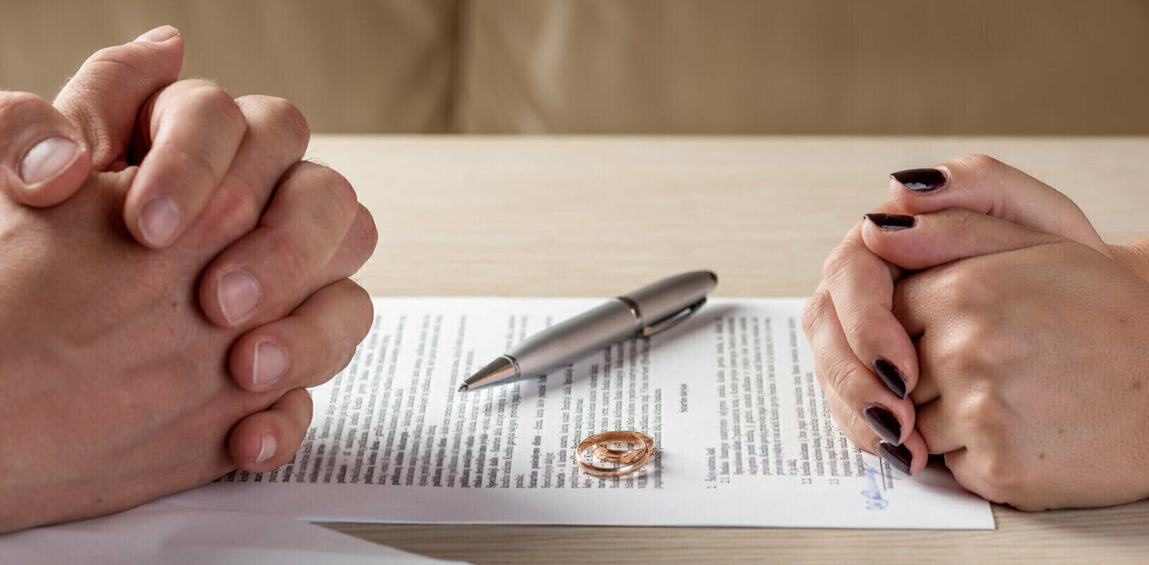 Two people getting divorced with paperwork on top of the table and wedding ring in the middle.