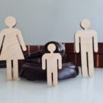Wooden family figures in front of judge’s gavel symbolizing child custody battle and parental rights dispute